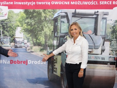 Zdjęcie przedstawia samorządowców stojących na tle zdjęcia z inwestycji remontu drogi