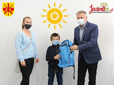 Zdjęcie przedstawia sekretarza Tomasza Podhoreckiego wręczającego plecak solarny Jasiowi Koskowi