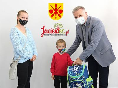 Zdjęcie przedstawia sekretarza Tomasza Podhoreckiego wręczającego Wojtkowi zestaw szkolny