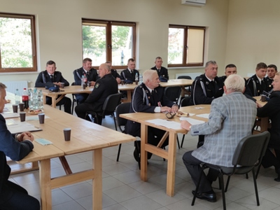 Zdjęcie ze spotkania OSP, przy stołach siedzący strażacy