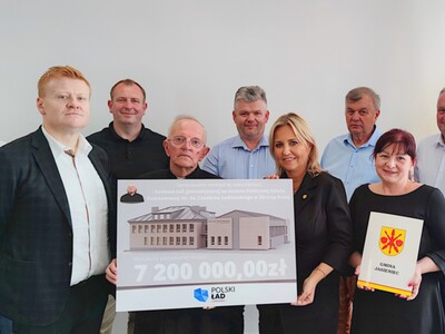 Podpisanie umowy na wykonanie inwestycji, na zdjęciu osoby trzymające czek i umowę