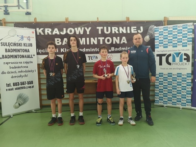 Na zdjęciu trener klubu wraz z zawodnikami udekorowanymi medalami. Na piersi jednego z chłopców widnieją dwa medale. Dwóch chłopców trzyma w rękach statuetki.