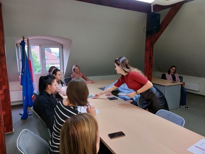 Pracownik Gminnego Punktu Konsultacyjno-Informacyjnego rozdaje ulotki uczestnikom spotkania.