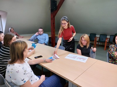 Pracownik Gminnego Punktu Konsultacyjno-Informacyjnego rozdaje ulotki uczestnikom spotkania.