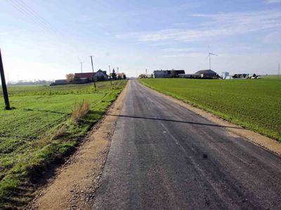 Zdjęcie na którym widać drogę asfaltową śródpolną prowadzącą pomiędzy gospodarstwami rolnymi a polami [400x300]