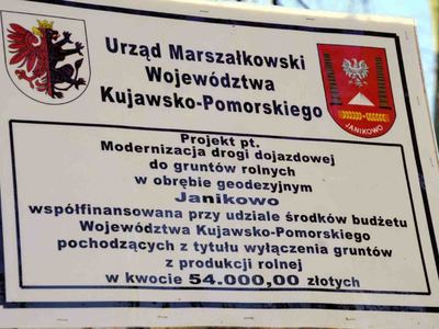 Zdjęcie białej tablicy informacyjnej z czarnymi napisami i 2 kolorowymi logami na której znajduje kolorowe Logo Urzędu Marszałkowskiego Województwa Kujawsko Pomorskiego i Logo Gminy Janikowo oraz informacja Projekt pt Modernizacja drogi dojazdowej do gruntów rolnych w obrębie geodezyjnym Janikowo współfinansowana przy udziale środków budżetu Województwa Kujawsko Pomorskiego pochodzących z tytułu wyłączenia gruntów z produkcji rolnej w kwocie 54 00000 złotych [400x300]