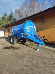 Zdjęcie niebieskiego beczkowozu na tle pomarańczowego budynku.