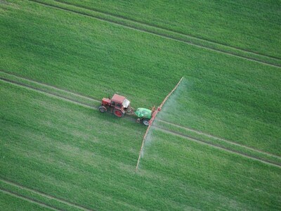 Zdjęcie przedstawia traktor i opryskiwacz jadące po zielonym polu uprawnym