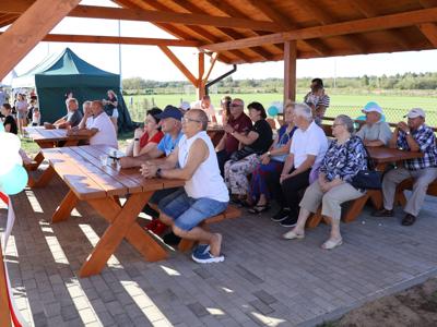 Uczestnicy siedzą w ławeczkach pod namiotem
