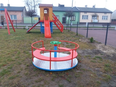 Na pierwszym planie bujawka obrotowa, w tle zjeżdżalnia w formie domku.