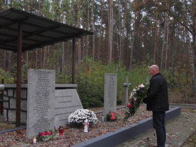 Zdjęcie przedstawia mogiłę zbiorową ogrodzoną płotem usytuowaną w lesie,