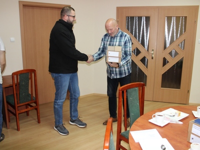 Wewnątrz. Dwie osoby stoją. Jedna drugiej wręcza paczkę.