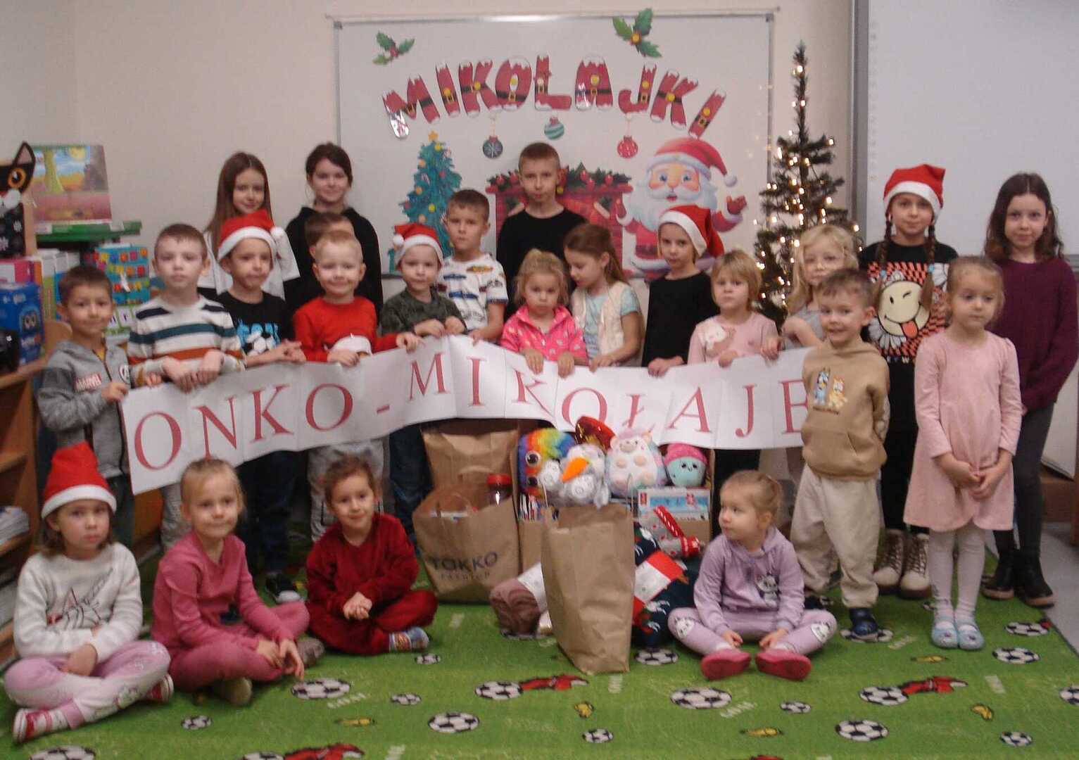 Grupa dzieci pozująca do zdjęcia z napisem ONKO-MIKOŁAJE. Wewnątrz.