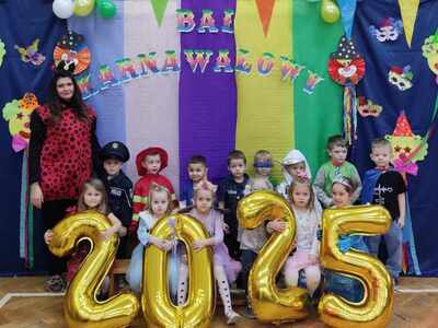 Grupa dzieci i pani w strojach karnawałowych pozują do zdjęcia. Wewnątrz.