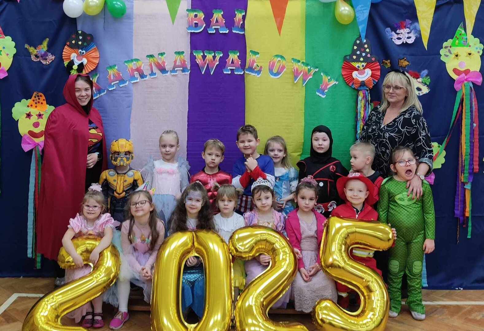 Grupa dzieci i dwie panie w strojach karnawałowych pozują do zdjęcia. Wewnątrz.