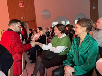 zdjęcie wykonane wewnątrz pomieszczenia. Na zdjęciu widoczny artysta wykonawca przechadzający się wśród widowni.