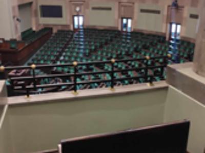Zdjęcie wykonane wew. pomieszczenia . Na zdjęciu widoczna kobieta , w tle godło RP oraz flagi RP i UE.