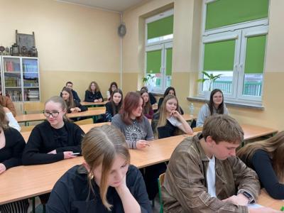 Grupa młodzieży siedząca w szkolnych ławkach. Wewnątrz.