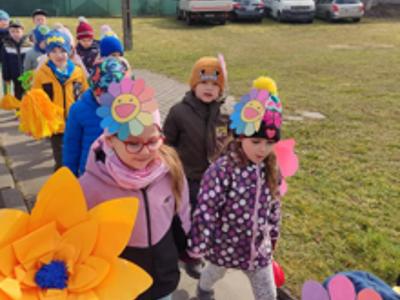 Grupa dzieci maszerująca z kwiatami. Na zewnątrz.