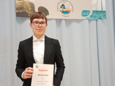 Uczeń pozuje do zdjęcia z dyplomem. Wewnątrz.