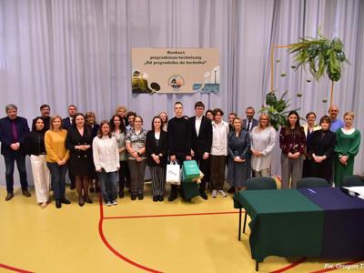 Grupa osób – uczniowie i nauczyciele pozujący do zdjęcia. Wewnątrz.