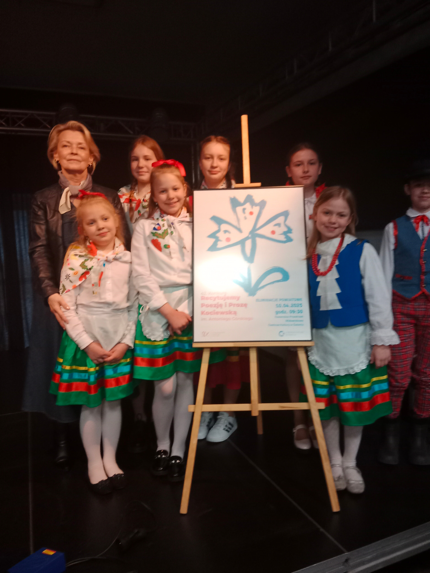 Grupa dzieci i pani pozujący do zdjęcia. Wewnątrz.