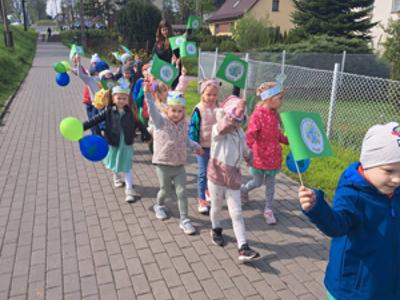 Dzieci maszerują trzymając chorągiewki i balony. Na zewnątrz.