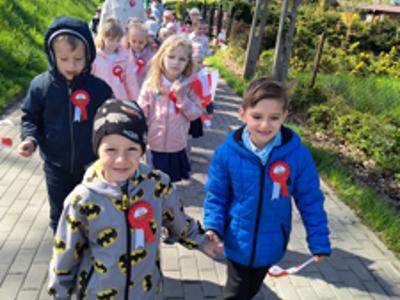 Grupa dzieci i nauczyciele idący w „Biało-czerwonym marszu”. Na zewnątrz.