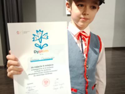 Chłopiec pozujący do zdjęcia z dyplomem. Wewnątrz.