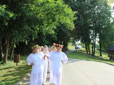 grupa osób ubranych na biało z wiankami na głowie tańczy poloneza