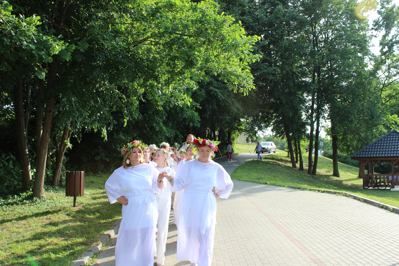grupa osób ubranych na biało z wiankami na głowie tańczy poloneza