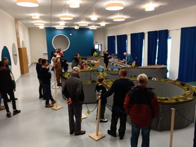 Grupa ludzi oglądająca makietę z kolejkami. Wewnątrz