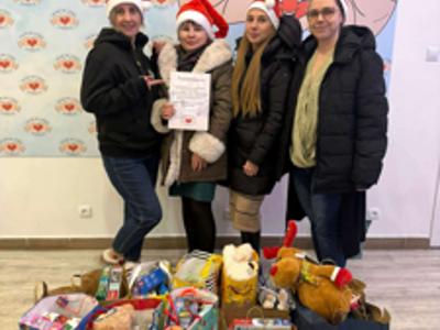 Cztery kobiety w czapkach Mikołaja pozujące do zdjęcia przy torbach z prezentami. Wewnątrz.