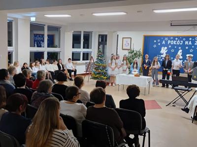 Grupa osób oglądająca przedstawienie przygotowane przez dzieci. Wewnątrz.