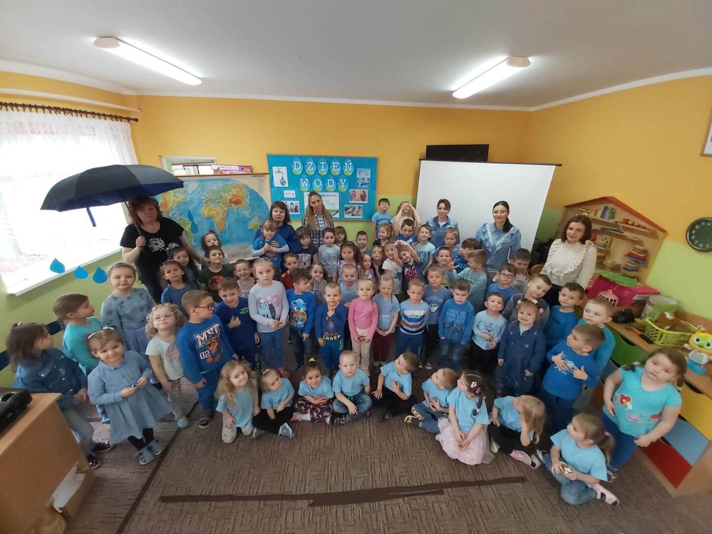 Grupa dzieci z opiekunami pozująca do zdjęcia. Wewnątrz.