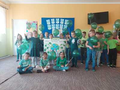 Grupa przedszkolaków ubrana za zielono, dzieci trzymają zielone balony. Wewnątrz.