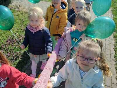Grupa przedszkolaków maszeruje z balonikami. Na zewnątrz.