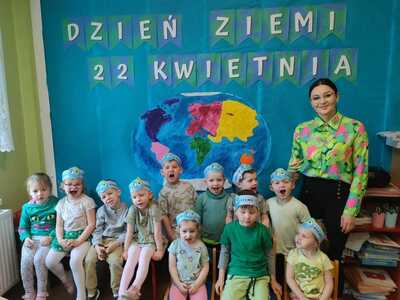 Grupa przedszkolaków z panią a nad nimi napis :” Dzień Ziemi 22 kwietnia”. Wewnątrz.