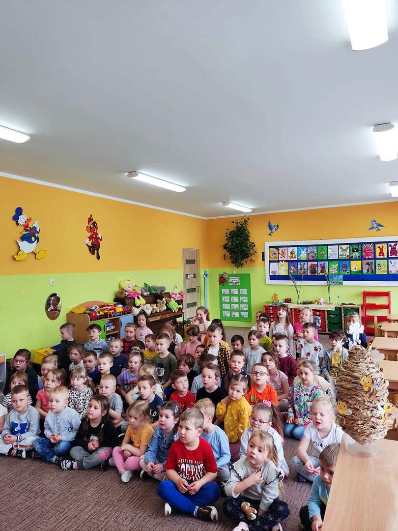 Grupa przedszkolaków słuchająca wykładu pszczelarza. Wewnątrz.