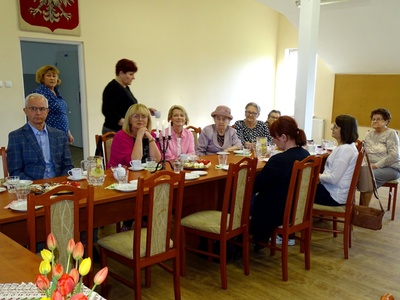 Grupa osób siedząca przy zastawionym stole podczas wykładu. Wewnątrz.