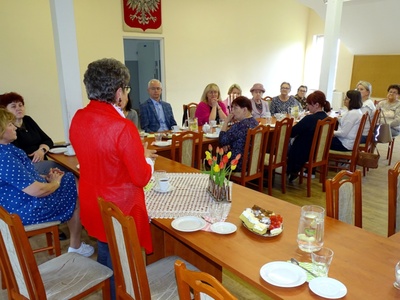Grupa osób siedząca przy zastawionym stole podczas wykładu. Wewnątrz.