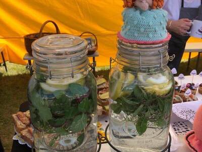 Na tle żółtej ściany namiotu widoczne dwa szklane słoje wypełnione wodą z miętą i cytryną. Na górze jednego z nich siedzi kolorowa lalka.