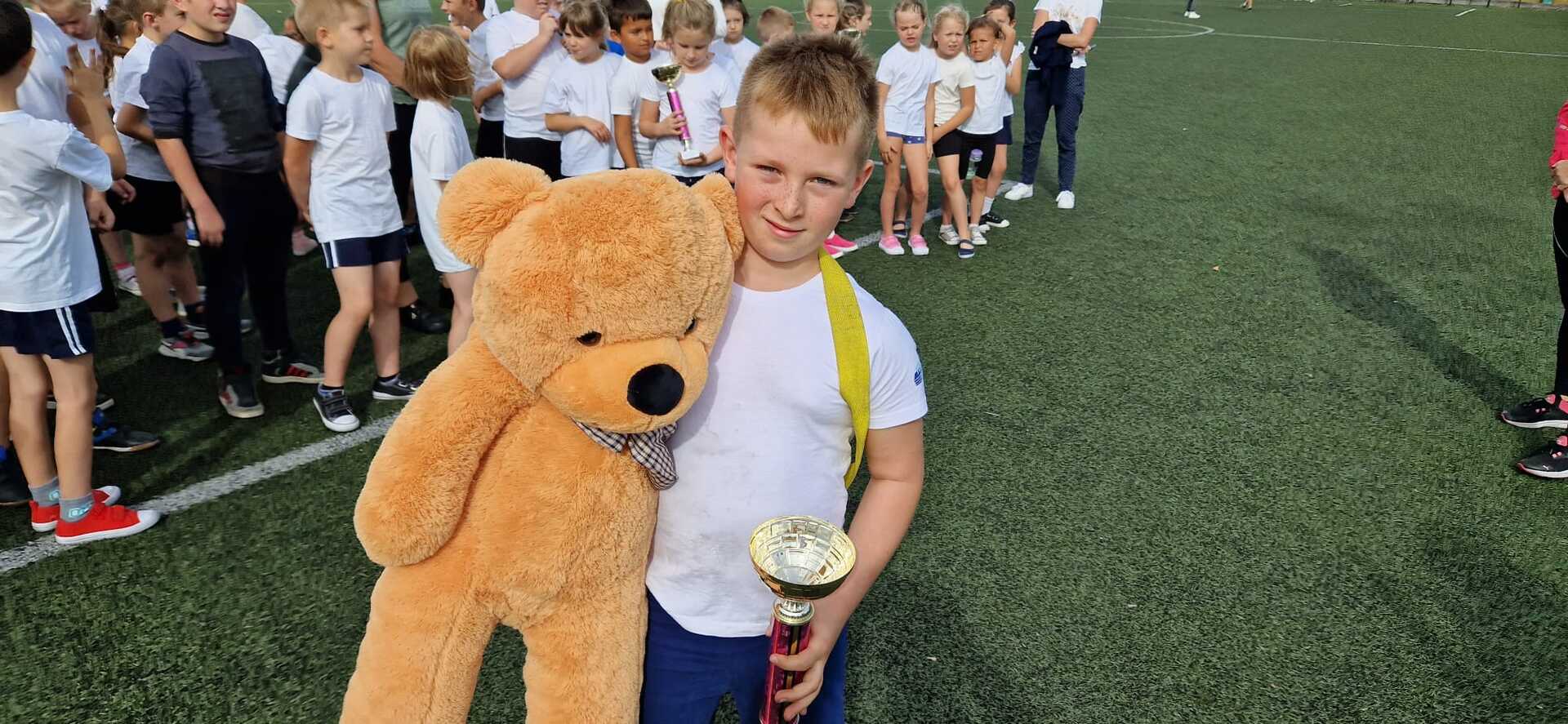 Chłopiec trzyma puchar i pluszowego misia. Na zewnątrz.