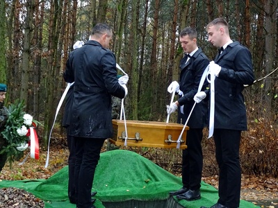 Pracownicy zakładu pogrzebowego składający trumnę ze szczątkami ekshumowanych żołnierzy w mogile.