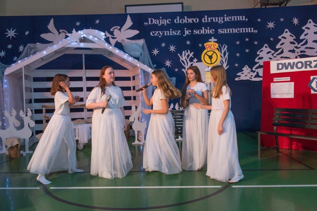 wewnątrz, na scenie występuje pięć dziewczynek w białych sukniach