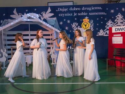 wewnątrz, na scenie występuje pięć dziewczynek w białych sukniach