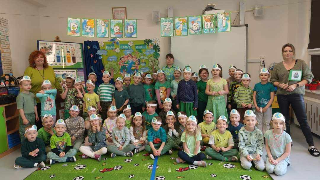 Grupa przedszkolaków z trzema paniami opiekunkami ubrana na zielono. Wewnątrz.
