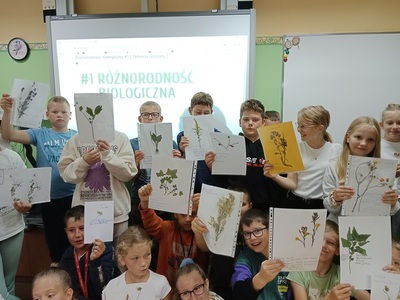 Grupa dzieci trzymająca kartki z zielnika. Wewnątrz.