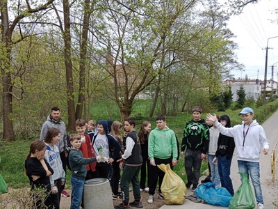Grupa dzieci z opiekunem w trakcie akcji zbierania śmieci. Na zewnątrz.