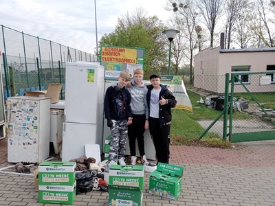 Trzech chłopców pozujących do zdjęcia przy elektrośmieciach. Na zewnątrz.